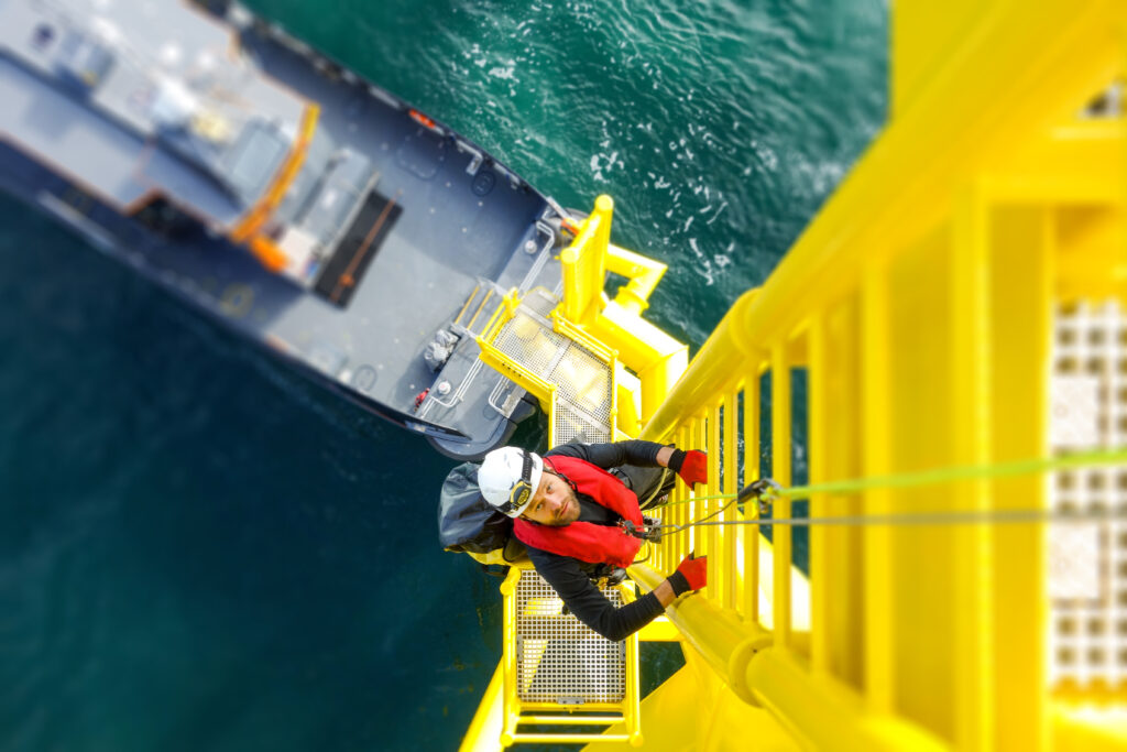 Manual high worker offshore climbing on wind-turbine on ladder. GWO Basic Safety Training
